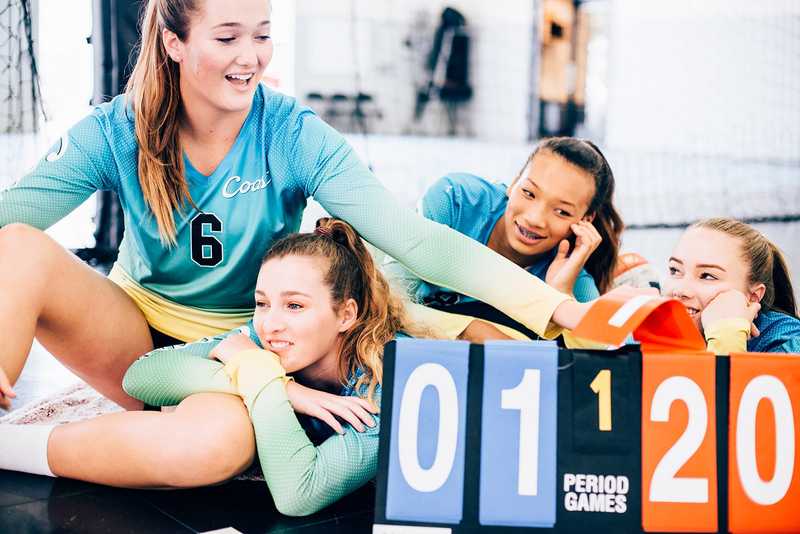Coast Volleyball athletes smiling together beside a scoreboard